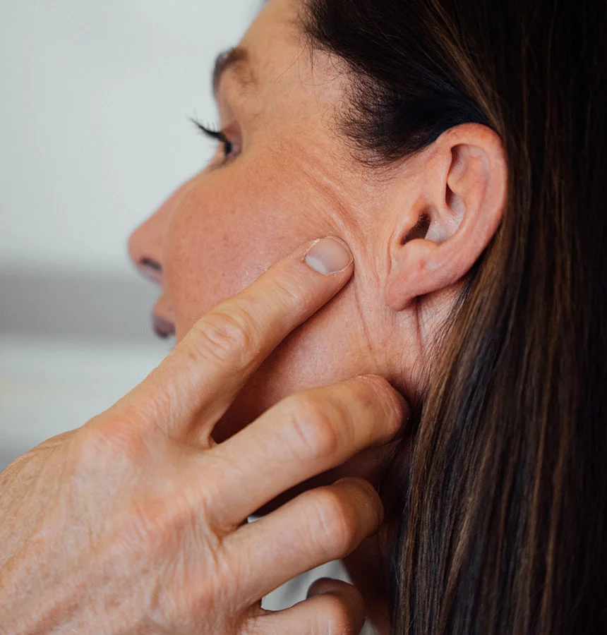 Close-up of a woman gently pulling back the skin near her jawline to highlight signs of aging and sagging skin along the lower face. - Mini Facelift in West Jordan, UT